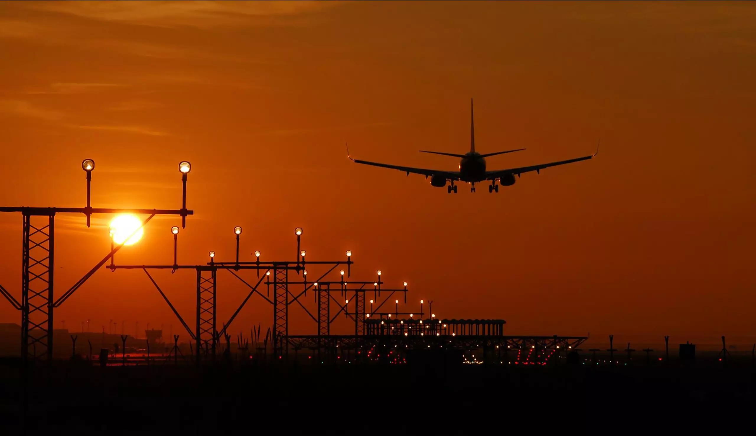 Silhouette of an airplane landing during sunset at Barcelona airport, with a vibrant orange sky.